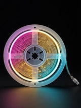 RGB LED strip light wound on a translucent reel and glowing pink, gold, and blue against black
