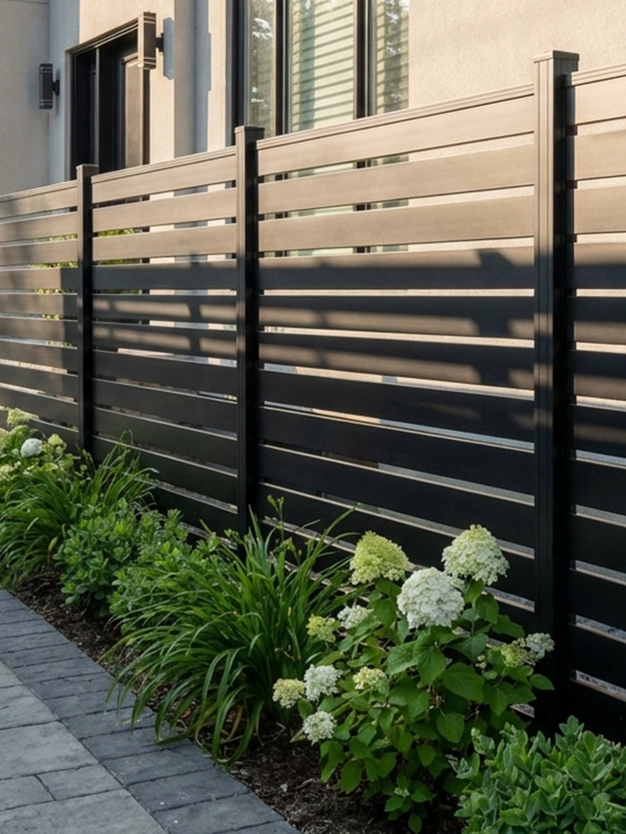 Connected black aluminum open slat fence panels installed along a landscaped garden