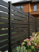 Black aluminum open slat fencing installed beside flowers and a modern home