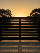 Silhouette of a slatted aluminum double gate against a golden sunset