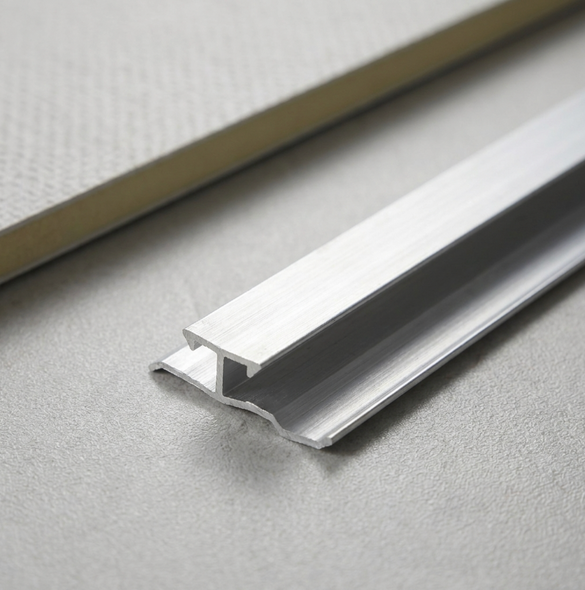 Close-up of silver aluminum trim connector profile with a raised center channel and side flanges