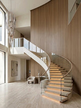 Bendable ash wood veneer panels wrapping a curved wall beside a sweeping staircase in a modern foyer