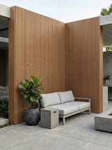 Brown composite wide exterior cladding with black grooves covering courtyard walls behind an outdoor sofa