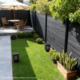 Black composite garden fence bordering a lawn with planters, lanterns, and outdoor dining furniture
