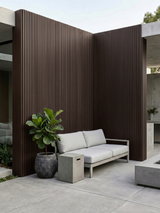 Dark brown composite wide exterior cladding covering tall patio walls behind a modern sofa and potted plant