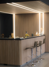 Bright white LED light strips installed across acoustic slat wall and ceiling panels in a home bar