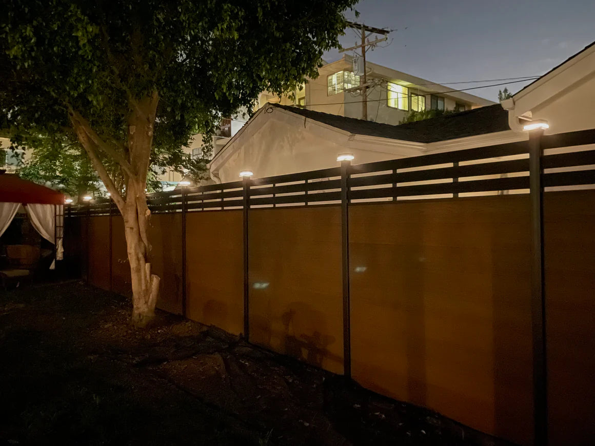 LED caps illuminating composite fence posts along a backyard fence at night