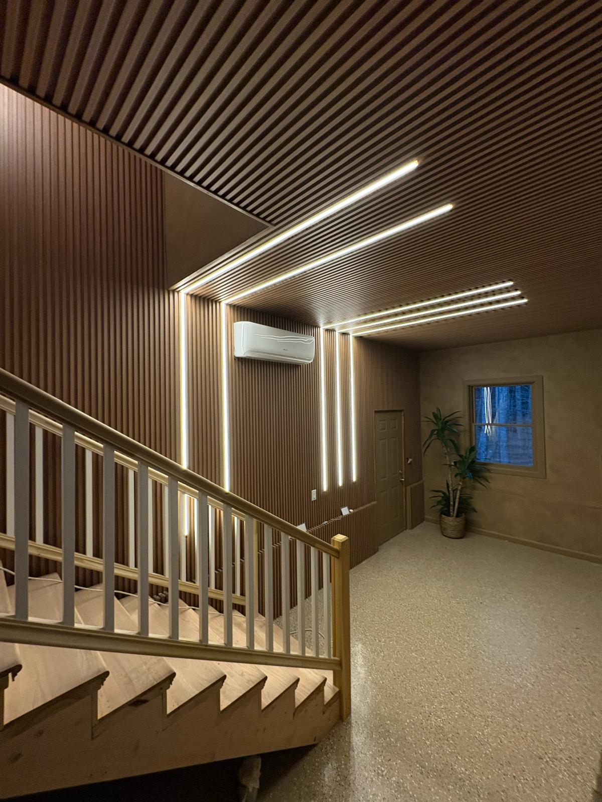 Warm white smart LED strip lights installed across a slatted ceiling and stairway wall