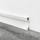 Close-up of white aluminum LED baseboard molding showing the open light channel beside gray tile flooring