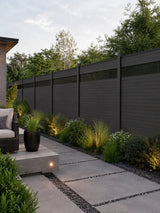 Modern decorative fence screens with narrow vertical slats installed along a dark fence beside a landscaped walkway