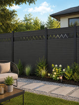 Modern decorative fence screen with dotted zigzag cutouts installed on a dark backyard fence beside a landscaped patio