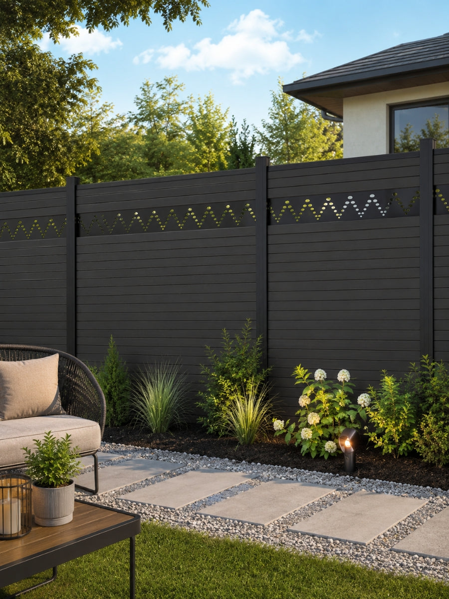 Modern decorative fence screen with dotted zigzag cutouts installed on a dark backyard fence beside a landscaped patio