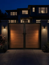 Brown WPC double fence gate installed between illuminated pillars outside a home at night