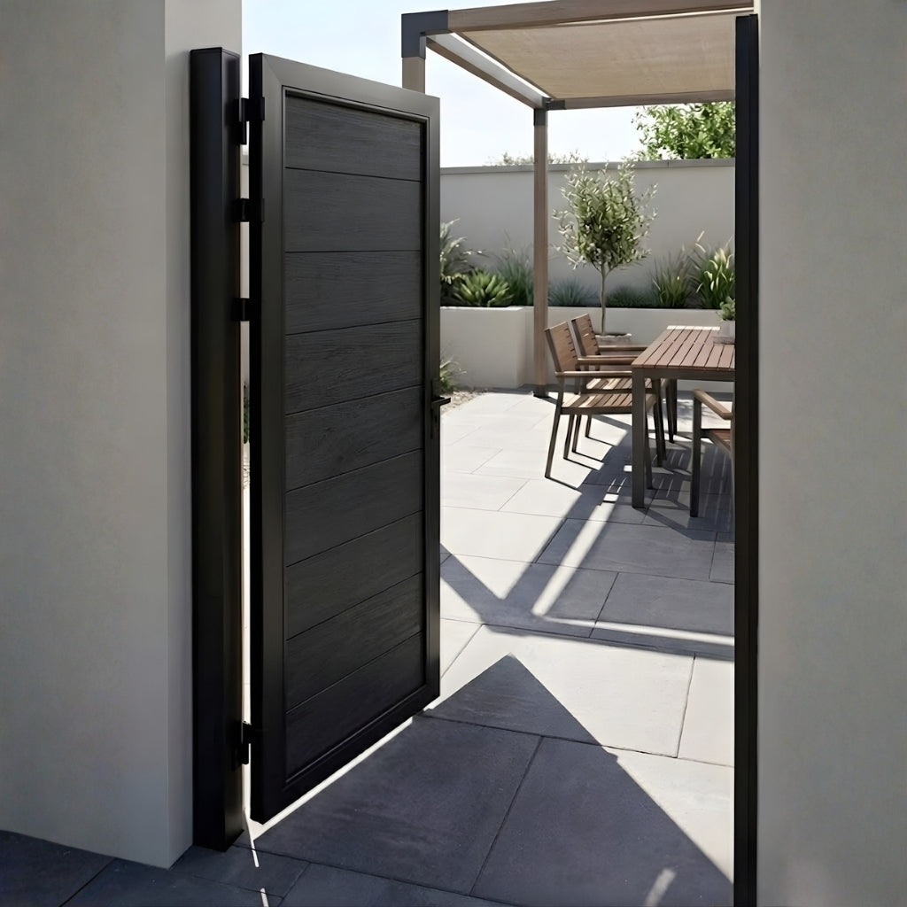 Open black WPC fence gate leading to a sunlit patio and outdoor dining area